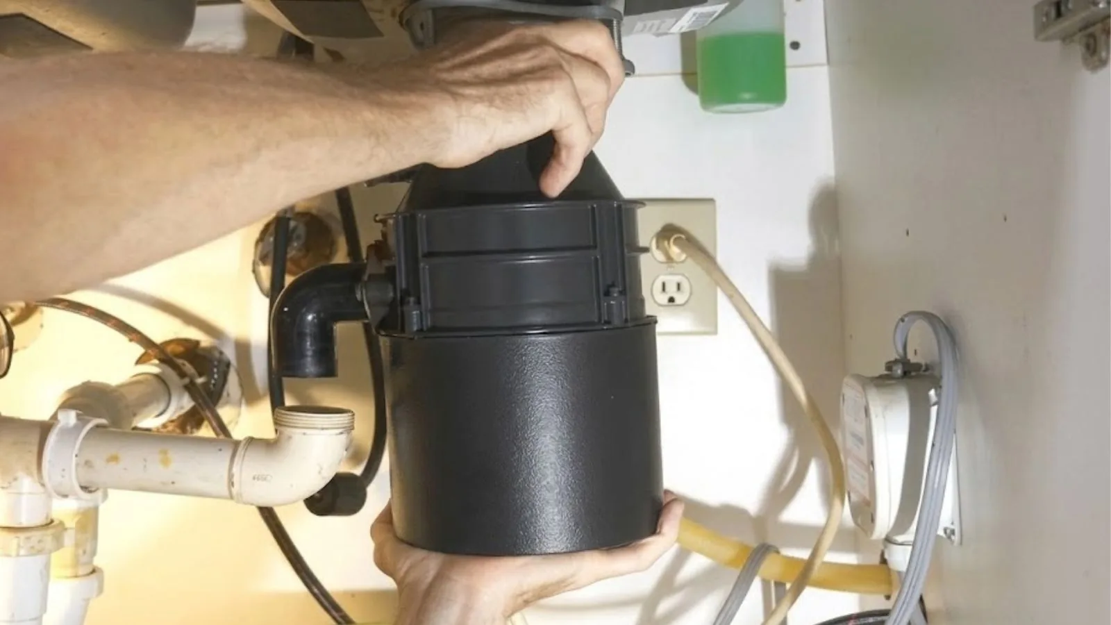 Hands installing a garbage disposal under a kitchen sink